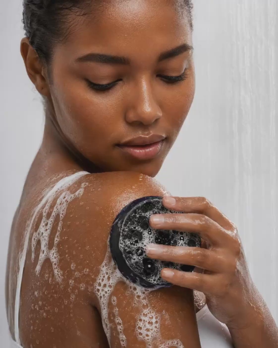 Person demonstrating the HueVine The Ingrown Hair Annihilator exfoliating bar during a shower skincare routine.
